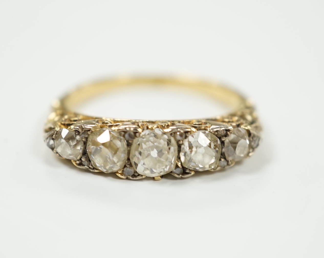 An early 20th century yellow metal and graduated five stone diamond set half hoop ring, with diamond chip spacers, size N/O, gross weight 4.7 grams.